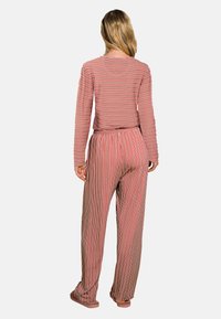 Gestreept loungepak in rood, crème en bruin. Langsleeve top en wijde broek met een elastische tailleband. Zachte textuur.