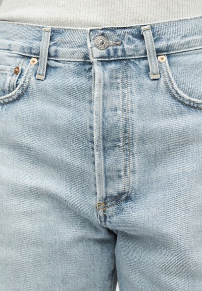 Ανοιχτό μπλε τζιν παντελόνι με κουμπιά μπροστά, θηλιές για ζώνη και εμφανείς ραφές, συνδυασμένο με λευκό τοπ με υφή.