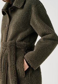 Getextureerde, donkergroene fleecejas met een ingesneden kraag, knoopsluiting, een ceintuur in de taille en een zijzak, met een zachte en gezellige uitstraling.