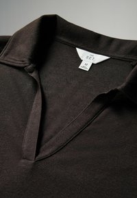 Polo shirt marrone scuro con texture a coste, dotato di un colletto a V e di un'etichetta con la scritta "THE SET" in taglia M.
