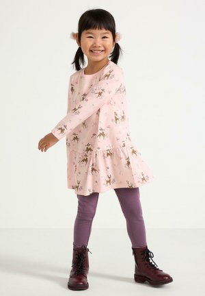 Vaaleanpunainen pitkähiha dressi, jossa on hirvi- ja kukkakuviot, levenevä helma, yhdistettynä purppurasiin legginsseihin ja mustiin nauhakenkiin.