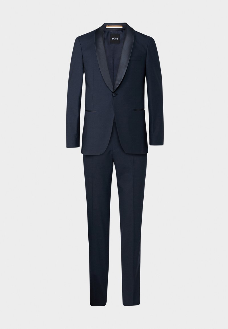 Costume bleu marine foncé avec un revers en satin, coupe slim, fermeture à un bouton, et pantalon assorti avec poches latérales.