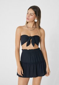 Czarny, strapless crop top z detalami w postaci węzła oraz pasującą, warstwową mini spódnicą. Lekki, teksturowany materiał z falbanami na dole. Srebrny naszyjnik z łańcuszkiem.