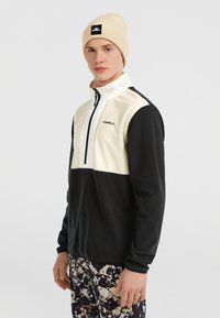 Zwart-wit ritsjack van fleece met hoge kraag en logo. Draag het met een broek met patronen en een beige beanie. Zachte textuur, sportief ontwerp.