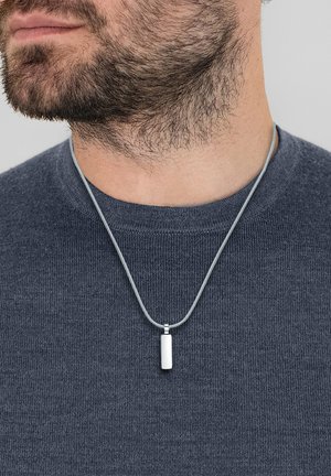 Hõbedane medaljong kaelakee hallil nööril, millel on ristkülikukujuline medaljon siledal pinnal, kantud tekstuurse halli sviitri peal.