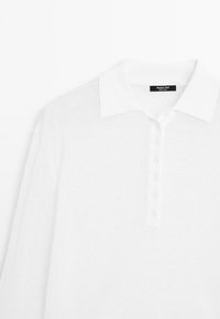Witte langekleurige poloshirt met een zachte textuur, voorzien van een geribde kraag, knopen aan de voorkant en een label met de merknaam.