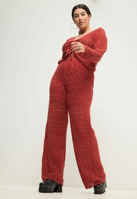 Completo a due pezzi all'uncinetto rosso caratterizzato da una maglietta con scollatura a V profonda e un fiocco, accompagnato da pantaloni a gamba larga, accentuati da un motivo testurizzato e ondulato.