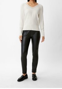 Jasnobeżowy sweter z dekoltem w serek i długimi rękawami, zestawiony z czarnymi spodniami ze sztucznej skóry. Całość uzupełniają czarne lakierowane loafersy.