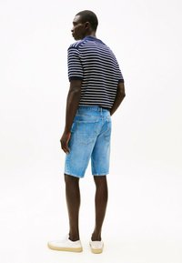 Polo a righe blu navy e bianche, pantaloni corti in denim azzurro, sneakers bianche. Il tessuto è liscio; i pantaloni corti hanno tasche posteriori e una vestibilità comoda.