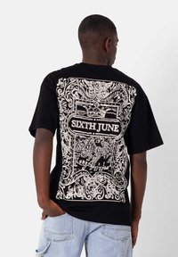 Camiseta de algodón negra con un gran diseño gráfico blanco en la parte posterior, con patrones intrincados y el texto "SIXTH JUNE". Mangas cortas.
