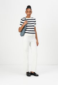 Gestreiftes Oberteil in Creme und Marineblau, kombiniert mit weißen, weit geschnittenen Hosen. Schwarze Loafers runden das Outfit ab. Die Tasche ist weich und grau.