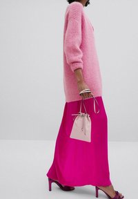 Różowy sweter dziewiarski o luźnym kroju, zestawiony z jasnoróżową spódnicą maxi. Posiada małą kremową torbę na sznurku oraz pasujące sandały na obcasie.