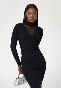 Black ribbed knit sweater with a mesh V-neck, accentuated by small embellishments, paired with a fitted black skirt and a silver handbag.