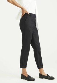 Black, cropped trousers with a smooth texture, featuring side pockets and rolled cuffs, paired with black leather loafers.