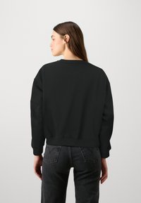 Felpa nera con vestibilità relaxed e collo a giro. Realizzata in tessuto morbido, presenta spalle scese e orlo a costine.