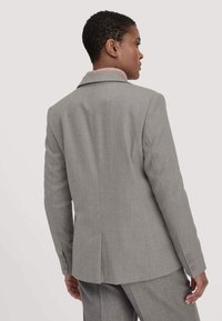 Grijze op maat gemaakte blazer met een reverskraag, een gestructureerde roze voering en manchetten met drie knopen. Beschikt over een getailleerd ontwerp en een zachte stof.