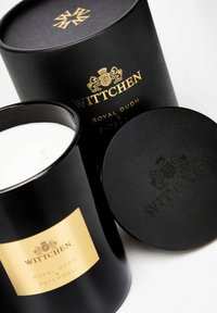 Contenitore di candela nera con etichetta dorata che riporta "WITTCHEN ROYAL OUDH & PATCHOULI", accompagnato da un coperchio nero abbinato con logo in rilievo.
