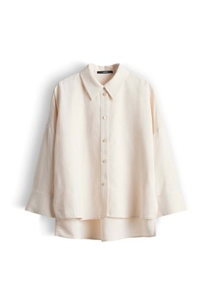 Camicia color crema a maniche lunghe con bottoni, colletto e orlo posteriore leggermente più lungo, mostrata su sfondo bianco.
