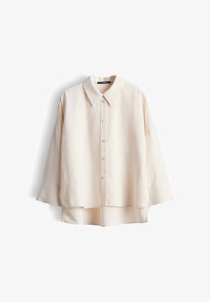 Camicia color crema a maniche lunghe con bottoni, colletto e orlo posteriore leggermente più lungo, mostrata su sfondo bianco.