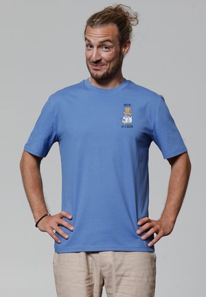 Blauwe katoenen t-shirt met korte mouwen heeft een cartoonhond in een doktersjas. De tekst luidt: "Vertrouw me, ik ben een dokter" onder het ontwerp.