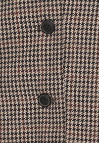 Tissu pied-de-poule marron, noir et blanc avec deux boutons noirs à quatre trous cousus en ligne verticale.
