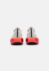 A Nike Air Max cipők fehér hálós felsőrésszel, piros buborék talppal és fekete részletekkel rendelkeznek. A hátulján egy húzófül és textúrázott talp található.