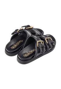 Sandali slide in pelle nera con cinturini a doppia fibbia, suola interna testurizzata e suola nera uniforme. Dettaglio del logo dorato sulla soletta.
