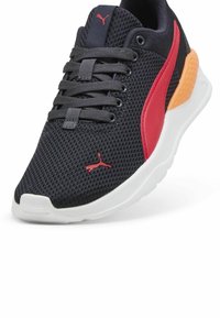 Baskets en mesh noires avec des accents rouges et orange, dotées d'une semelle blanche, d'un bout rond et d'un design à lacets avec un logo bien visible sur le côté.