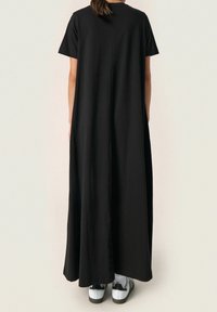 Czarna sukienka do kolan z krótkimi rękawami, o luźnym kroju i gładkiej fakturze, noszona z białymi i czarnymi sneakersami.