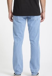 Jeans in denim azzurro chiaro con un taglio dritto, caratterizzati da due tasche posteriori e una leggera sbiaditura, abbinati a una t-shirt nera.