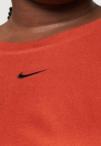 Röd bomull t-shirt med ribbad halsringning och svart Nike-logotyp broderad på bröstet. Tyget ser slätt och något elastiskt ut.