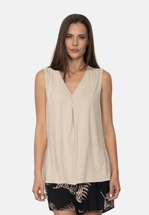 Top sin mangas beige con escote en V y fruncido en la parte delantera, hecho de un material suave, combinado con pantalones cortos negros con un patrón de hojas tropicales.