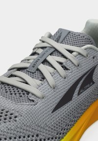 Γκρι δίχτυνο παπούτσι τρεξίματος Altra Escalante Racer με ανοιχτό γκρι κορδόνια και κίτρινη διαβαθμισμένη σόλα, κοντινό στο μπροστινό μέρος.