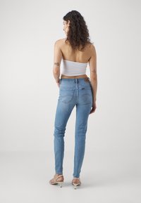 Tajta blå jeans i denim med hög midja, diskret sömnad och bakfickor. Kombineras med sandaletter och en vit topp.