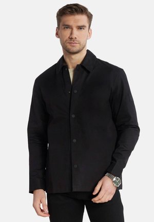 Giacca nera con chiusura a bottoni, maniche lunghe e colletto. Presenta una texture liscia e include un logo discreto sul braccio sinistro.