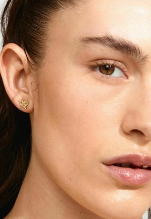 Goldene Schmetterlings-Ohrringe in Form eines Steckerohrrings am Ohr, mit filigranen Details, Nahaufnahme der Haut und sanften natürlichen Make-up-Tönen im Hintergrund.