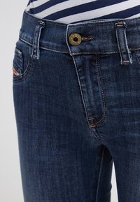 Mörkblå denimjeans med strukturerad yta, utrustade med knäppning av mässing och kontrasterande sömmar längs fickorna och sömmarna.
