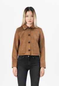 Giacca cropped in finta suede marrone con collo classico, chiusura a cinque bottoni e due tasche frontali. Il modello è abbinato a jeans neri.