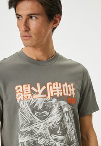 Grijze katoenen t-shirt met een grafische print van gestileerde gezichten in het wit en oranje. Ronde halsontwerp met korte mouwen.