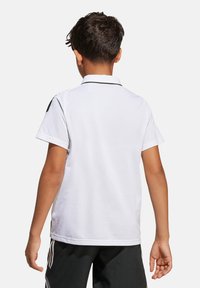Polo bianco con colletto nero e dettagli neri sulle spalle, maniche corte e tessuto liscio. Indossato con pantaloni sportivi neri.