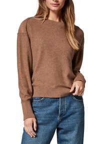 Bruine gebreide trui met een geribbelde ronde hals en manchetten, met een ontspannen pasvorm en een zachte structuur. Gecombineerd met blauwe denim jeans.