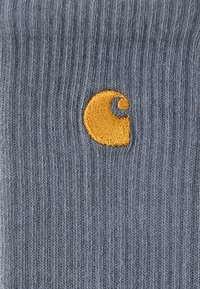 Γκρι πλεκτό ύφασμα με κάθετες ραβδώσεις, με κίτρινο κεντητό λογότυπο σε σχήμα σπείρας στο μπροστινό μέρος. Μαλακή υφή.