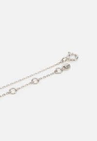 Bracciale in argento con piccoli anelli circolari, chiusura a gancio e un'etichetta a forma di cuore. Texture liscia con finitura lucida.