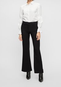 Vit skjorta med puffärm och långa ärmar, tillsammans med högmidjade svarta utsvängda byxor och svarta ankelskängor.