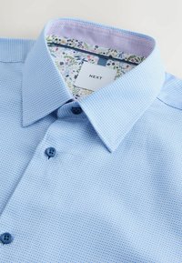 Hele sinise tooniga nööbitav särk tekstuurse pinnaga, kontrastse lillemustrilise sisemise kraega ja siniste nööpidega. Sildil on kiri "NEXT".