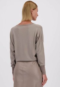 Licht taupe trui met een ontspannen pasvorm, lange mouwen en geribde manchetten. Vrijwel zachte textuur met een iets verkorte zoom en brede halslijn.