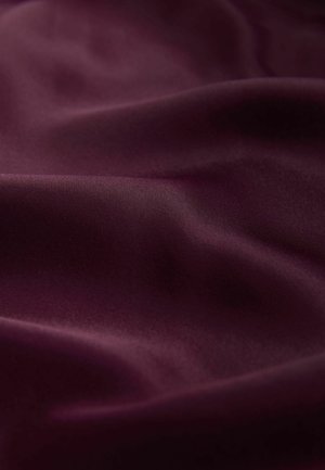 Weinroter Stoff mit einer glatten, leicht glänzenden Textur. Das Material wirkt weich mit sanften, fließenden Wellen auf der Oberfläche.