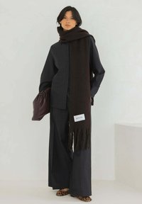 Chemise à rayures sombres, pantalon à jambe large, écharpe oversized marron avec des franges, et une pochette bordeaux, assortis à des ballerines imprimées léopard.
