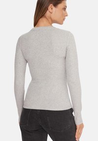 Top grigio a maniche lunghe in materiale morbido con design aderente, caratterizzato da scollo rotondo e texture liscia, abbinato a jeans scuri.