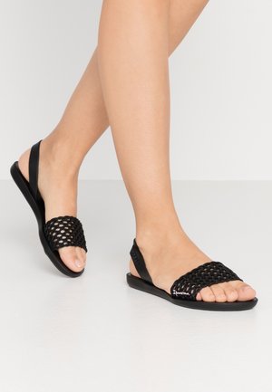 Sandales noires avec un design en maille tissée, semelle plate et sangle réglable. Fabriquées en matériau flexible avec un détail de marque subtil.